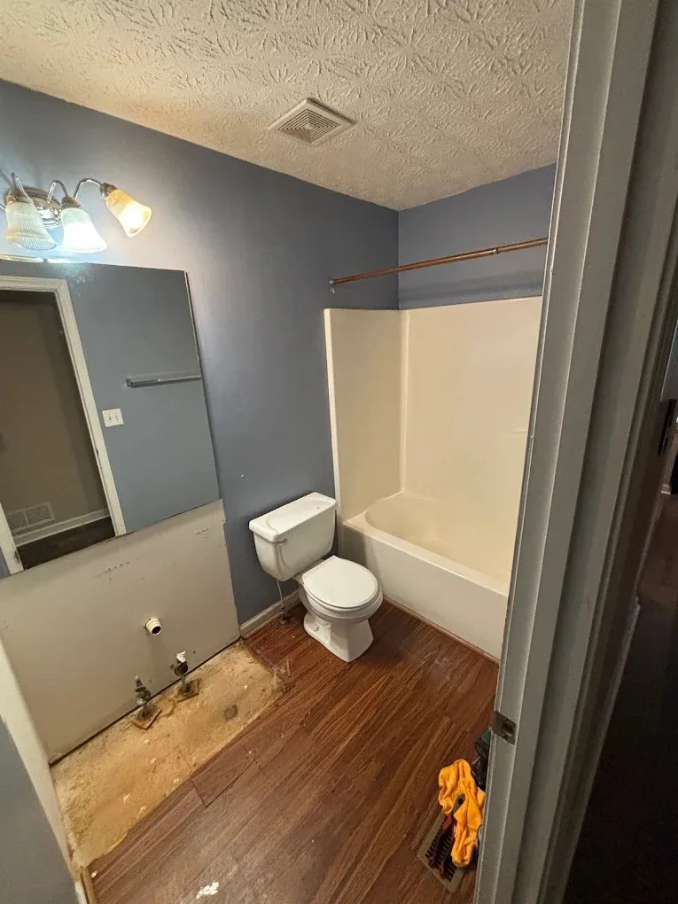 The same bathroom before the work: a tub and shower combo, an old vanity and blue walls