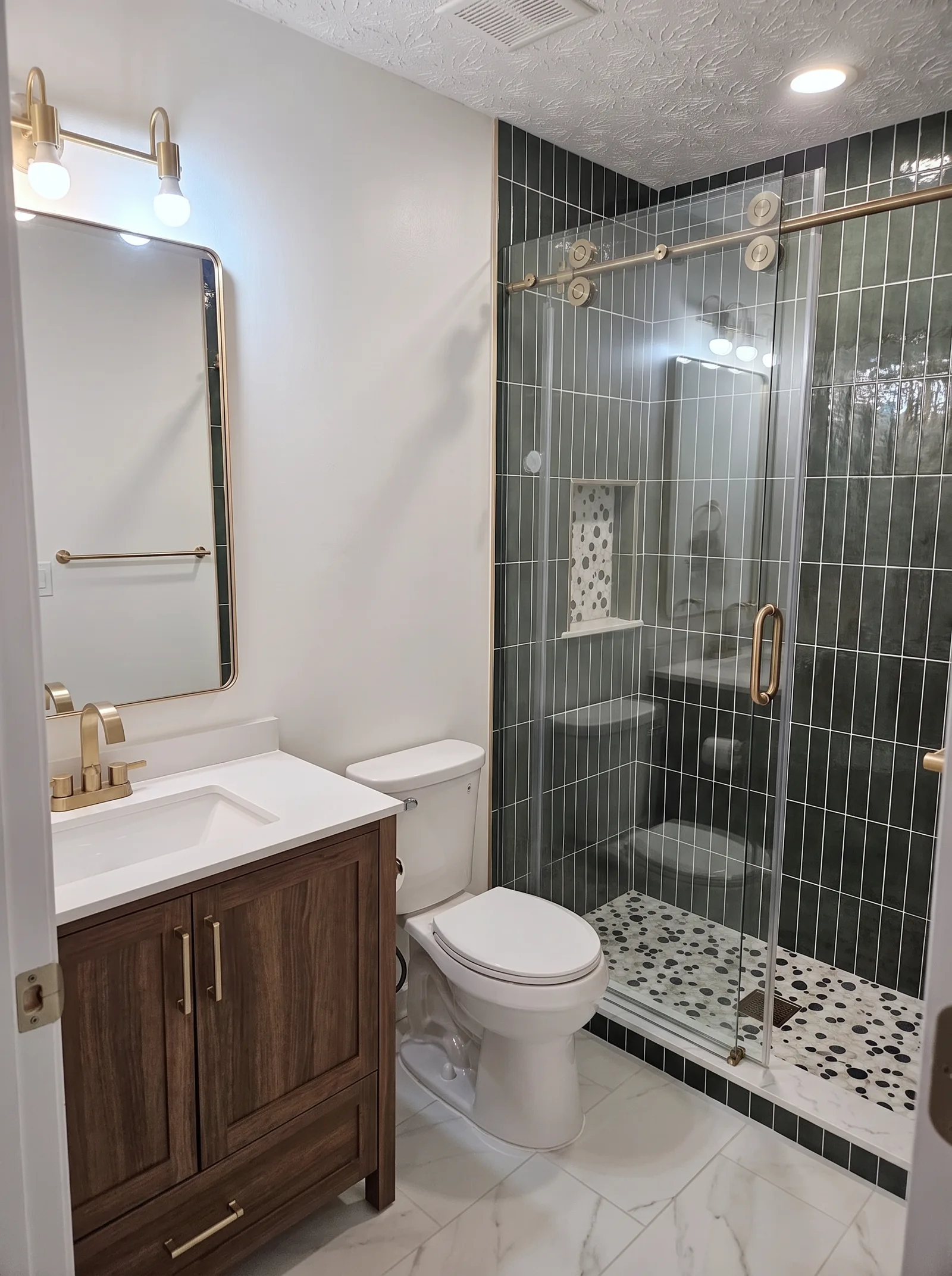 Bathroom with a walnut vanity, brass fixtures and a walk-in shower in deep green tile