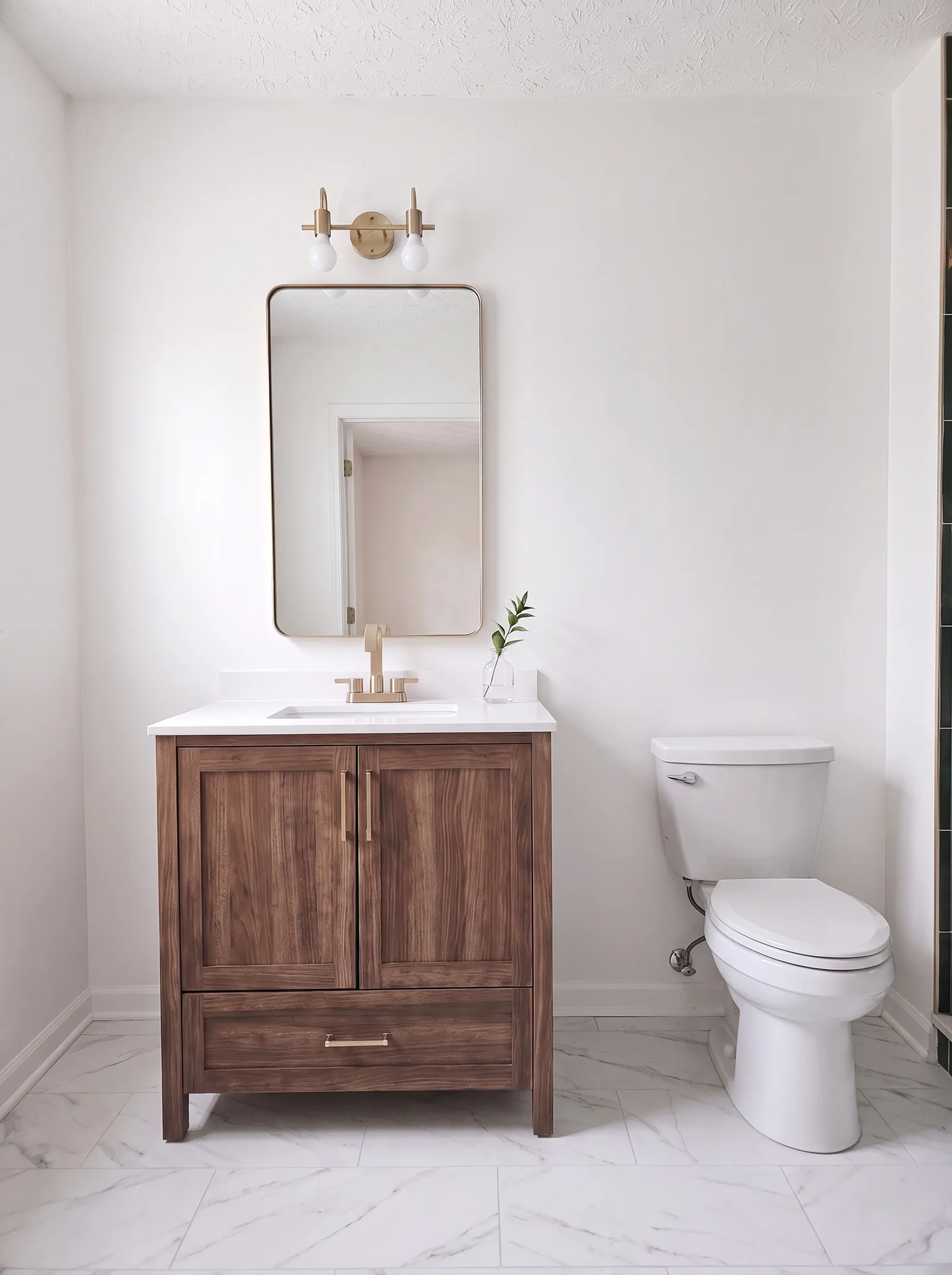 Walnut vanity with a white quartz top, brass faucet, brass-framed mirror and a two-light sconce