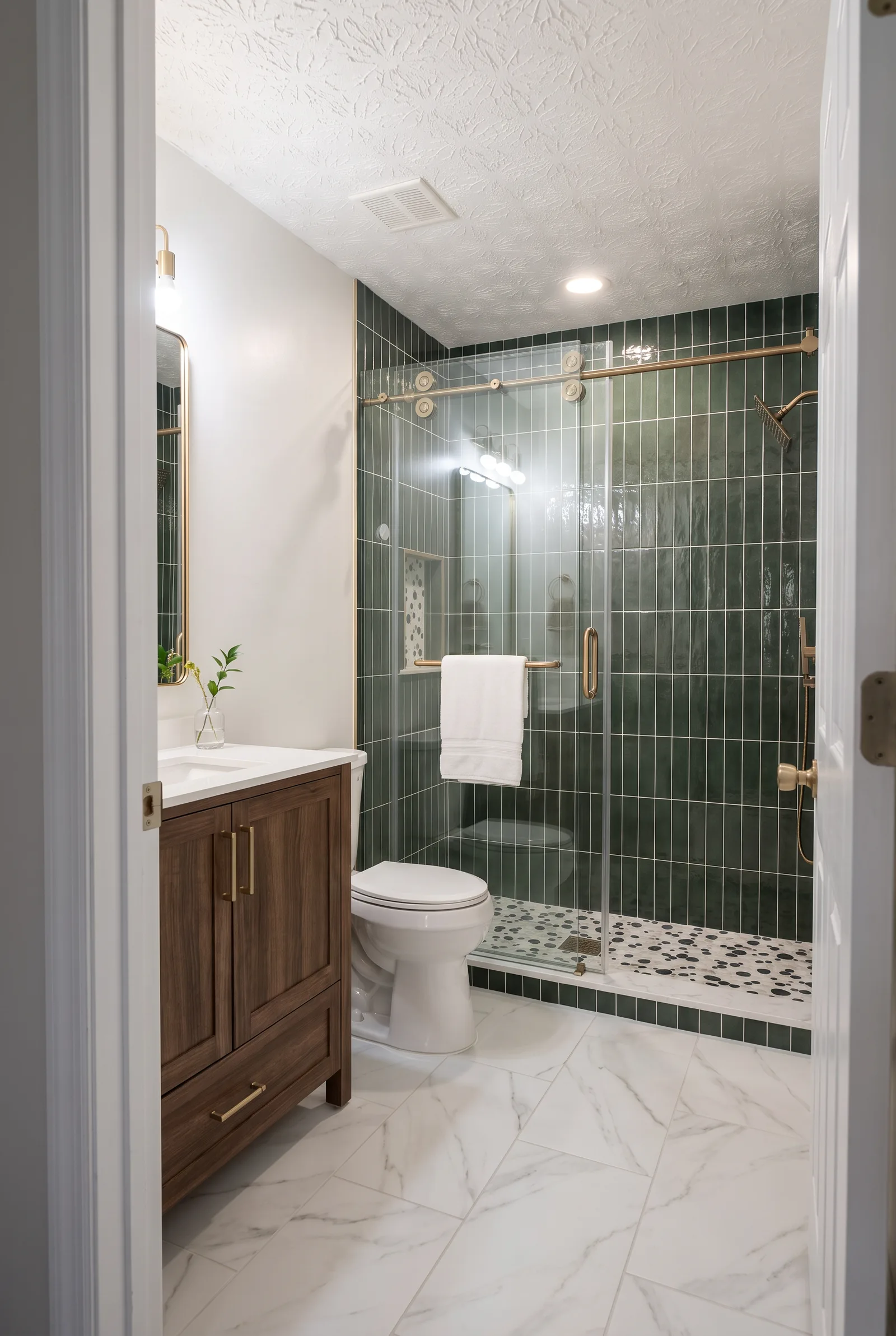 The bathroom seen from the hall through the open door, marble-look floor tile leading to the green shower