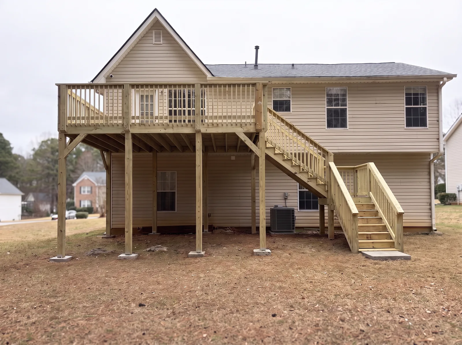 The deck straight on from the yard: square wood pickets, four support posts on concrete pads and the stairs at the right