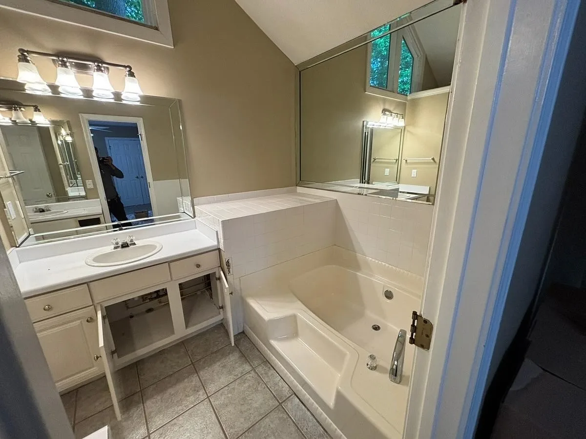 The same bathroom before the work: a built-in tub in a white tile deck, wall mirrors and an old vanity
