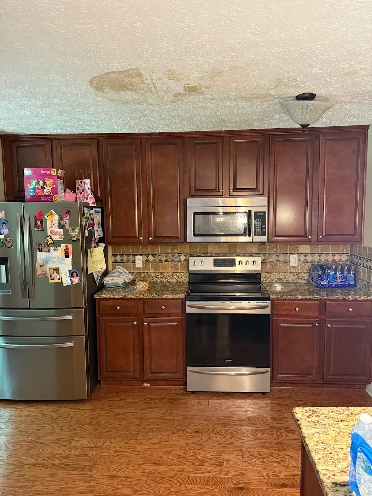 The same kitchen before the work: dark wood cabinets, granite counters and a water-stained ceiling