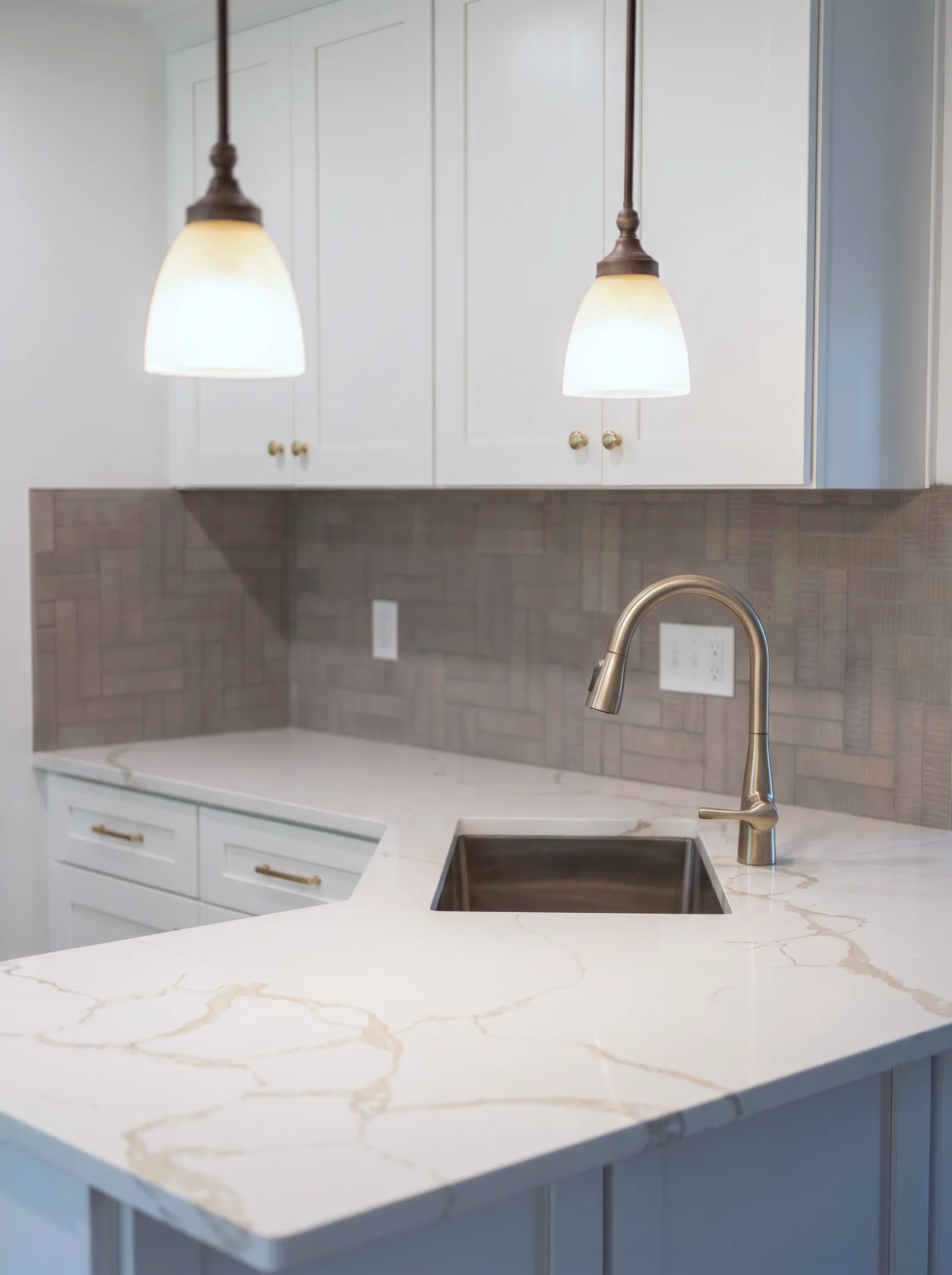 Champagne-gold faucet and stainless sink set in gold-veined quartz, basketweave tile behind